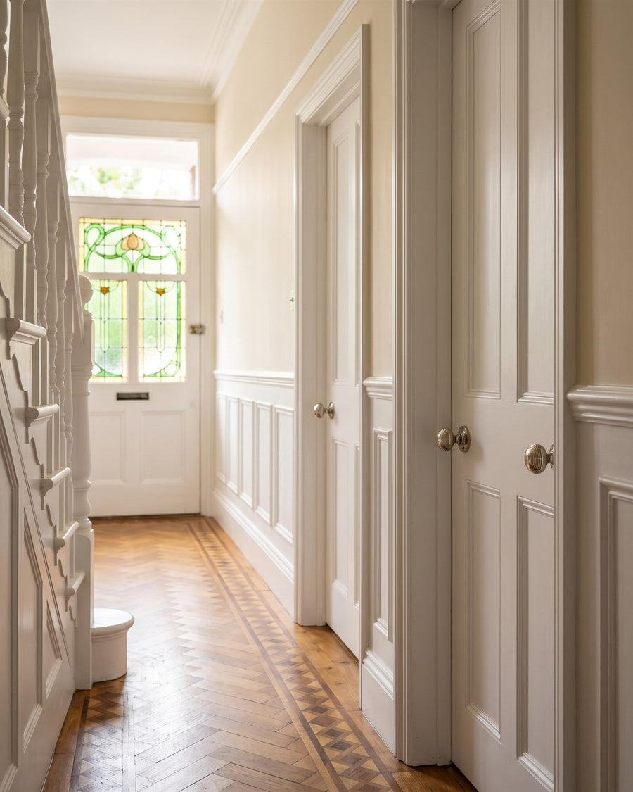 Light Edwardian hallway with cream walls, a picture rail, parquet floor and white four-panel doors with polished nickel reeded knobs