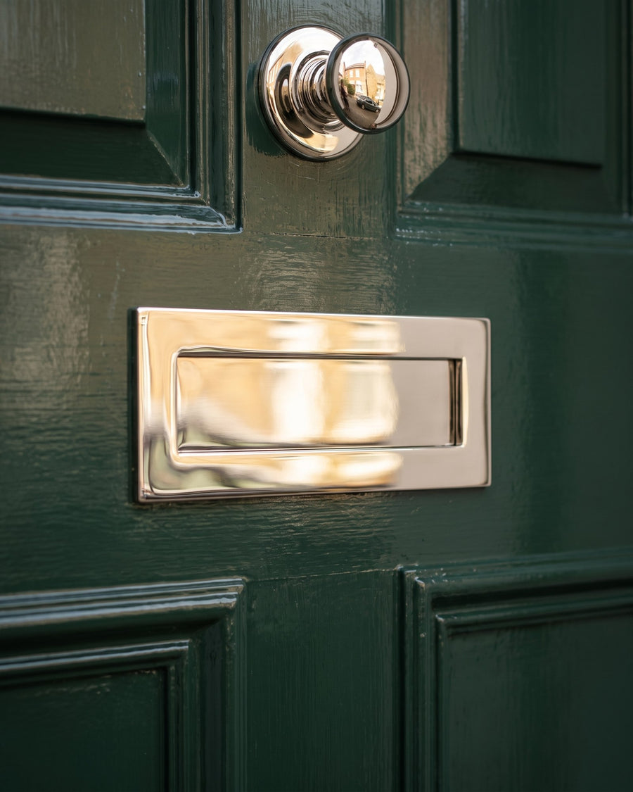 Polished nickel letter plate on the middle rail of a gloss deep green door with the centre knob above