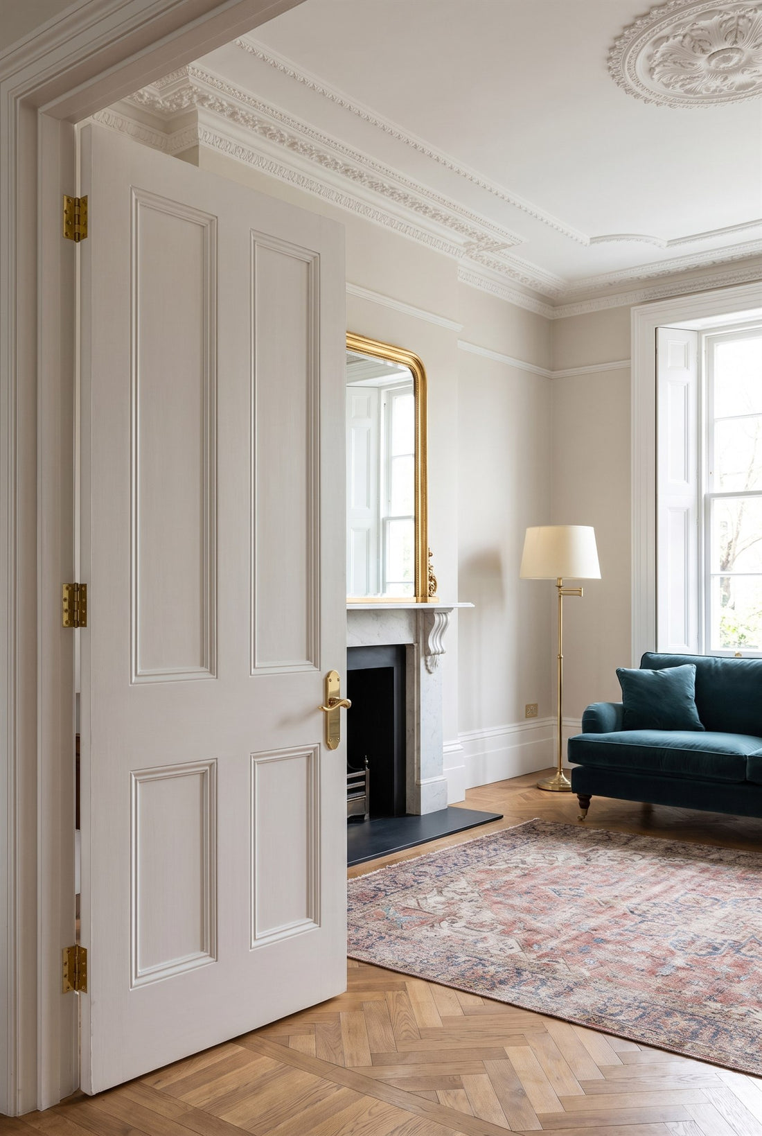 Edwardian mansion flat drawing room with cornicing, parquet and a marble fireplace, and a tall white door with a polished brass Savoy scroll lever and brass hinges