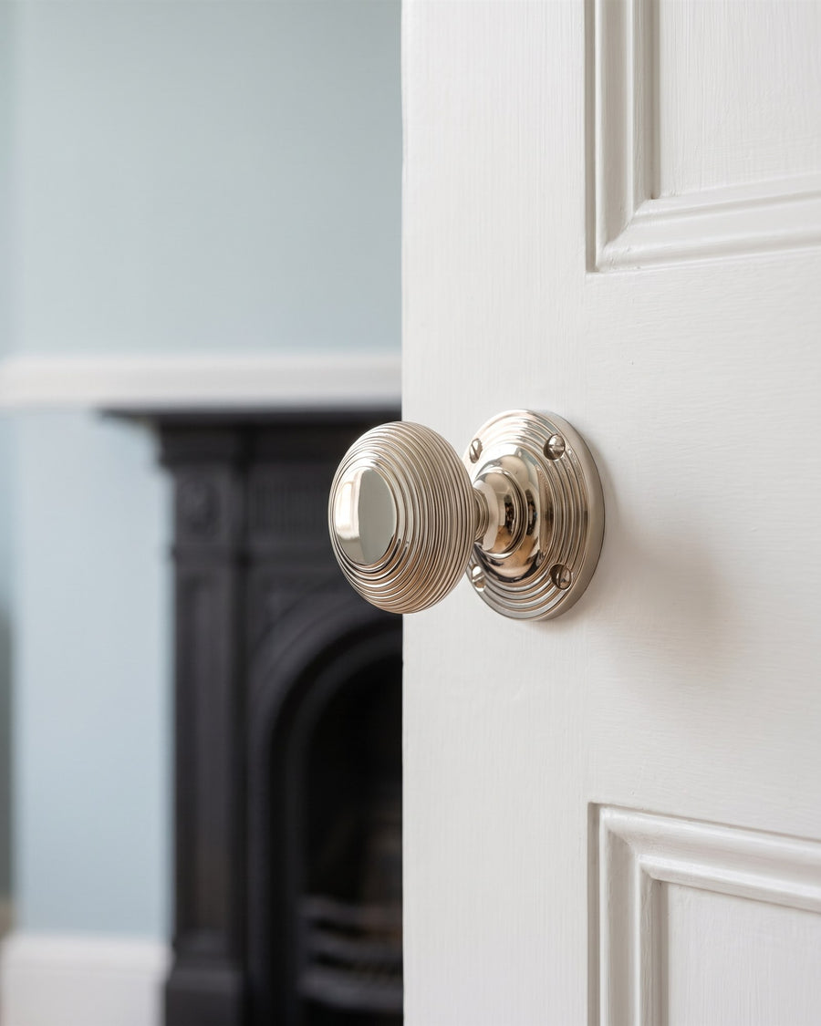Polished nickel reeded mortice knob on a white four-panel door, pale blue sitting room beyond