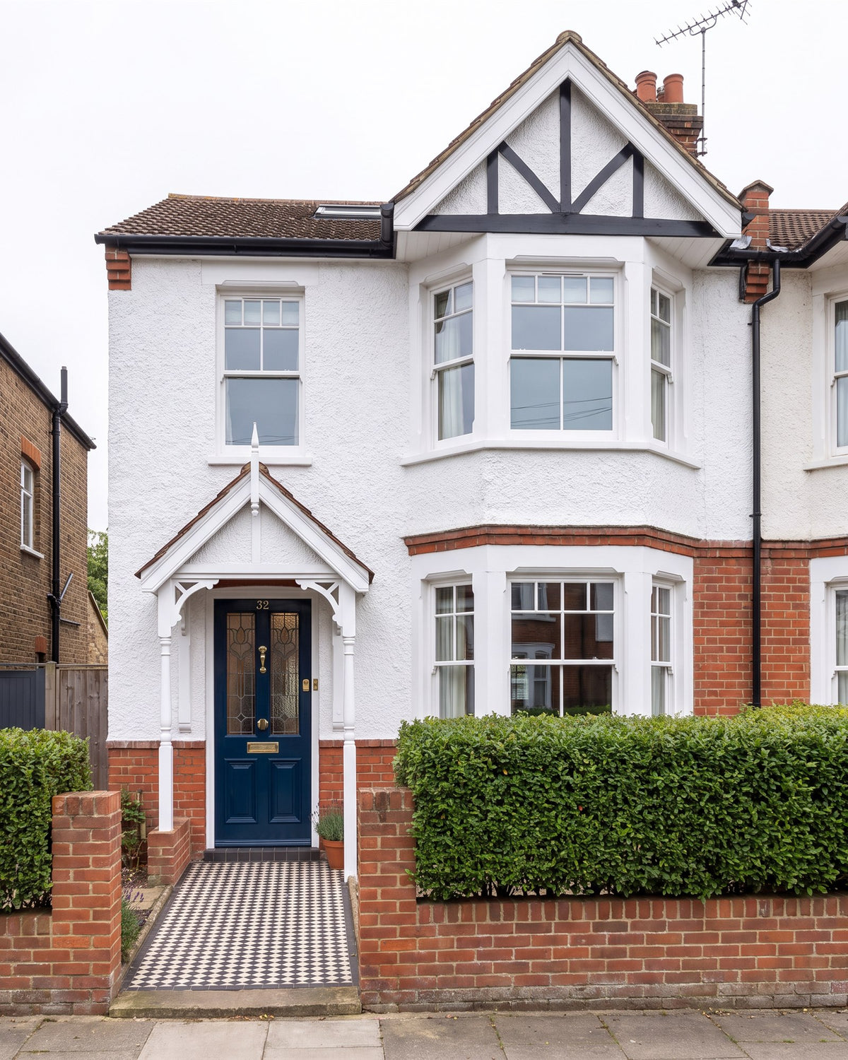 Edwardian semi with red brick, white roughcast and a mock-Tudor gable, a timber fretwork porch over an inky blue front door with stained glass and a chequerboard tiled path