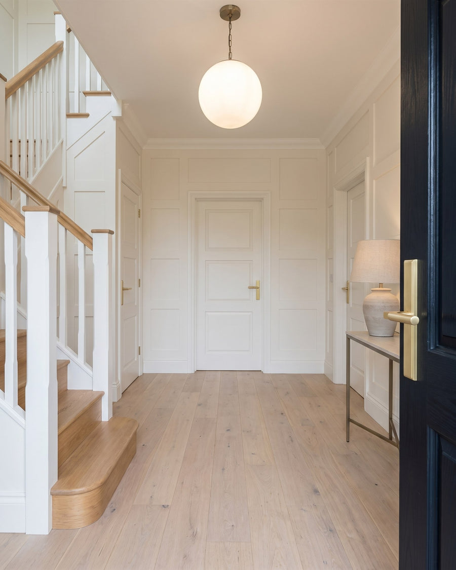 Bright entrance hall with an oak staircase, white spindles and warm white doors with satin brass Bauhaus levers, seen past the open front door and its multipoint handle