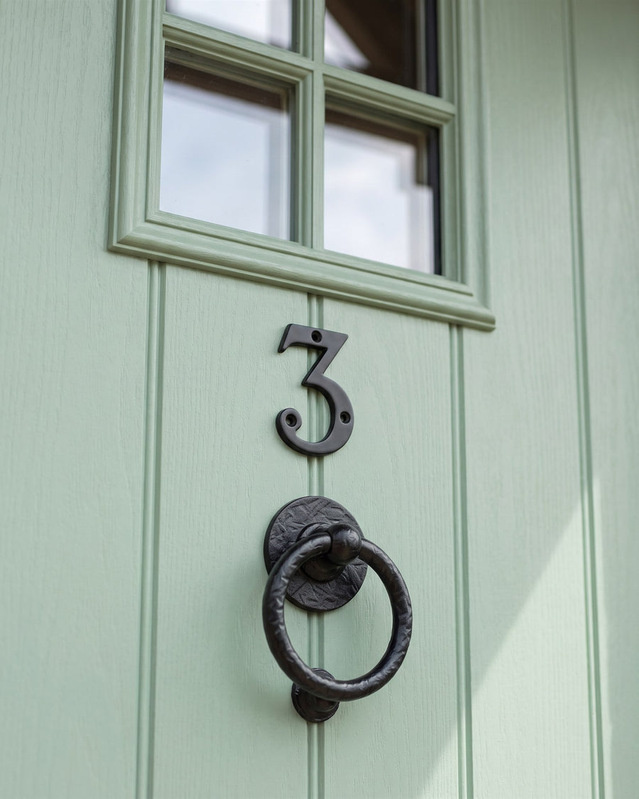 Black serif number 3 above a hammered forged black bull ring knocker on a heritage green boarded door