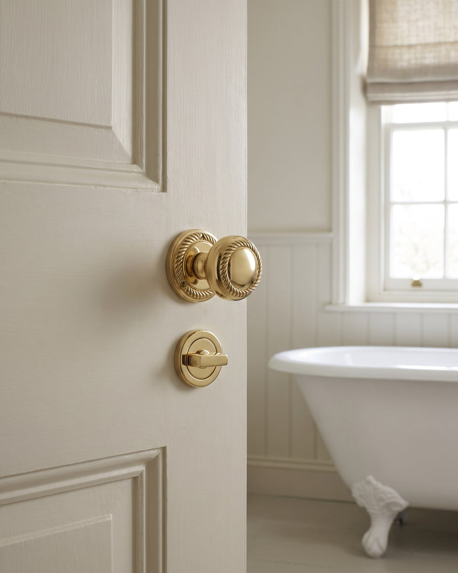 Georgian bathroom door with a polished brass rope-edge knob and a matching bathroom turn below it, roll-top bath behind