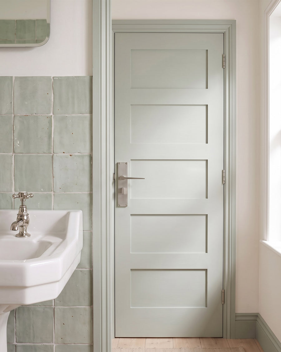 Inside of a closed sage bathroom door with the satin nickel Gio reeded bathroom handle and its rectangular thumbturn, beside pale green handmade tiles and a white basin