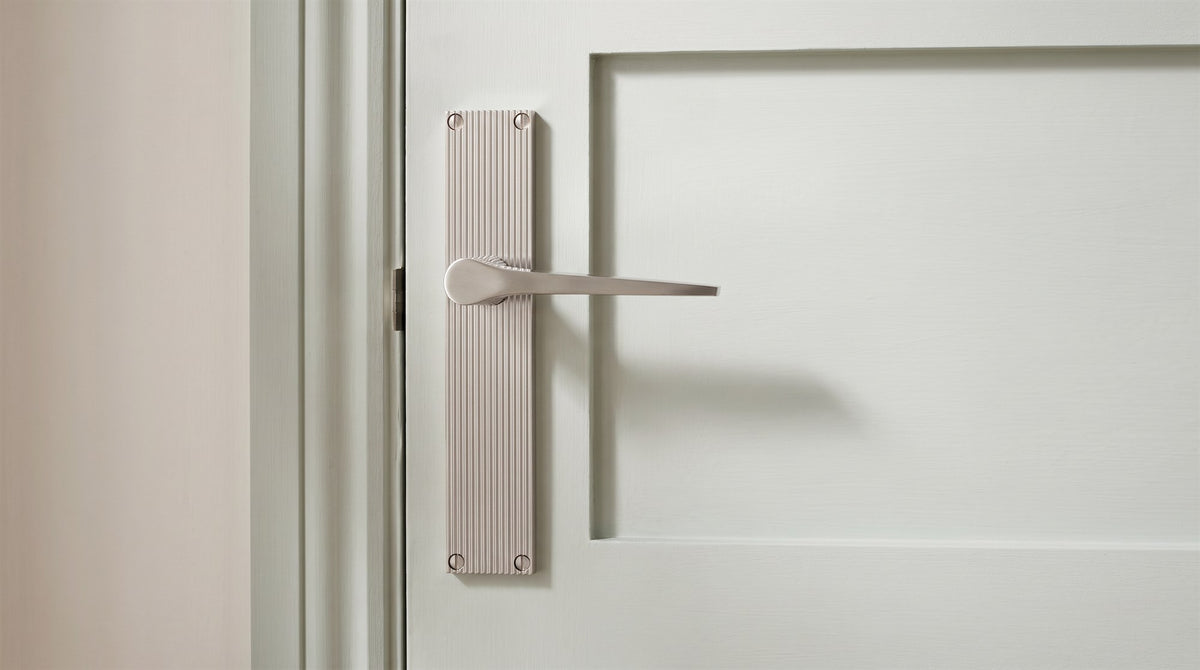 Satin nickel Gio lever with a slim angular blade on a finely reeded backplate, on a silvery sage green panelled door