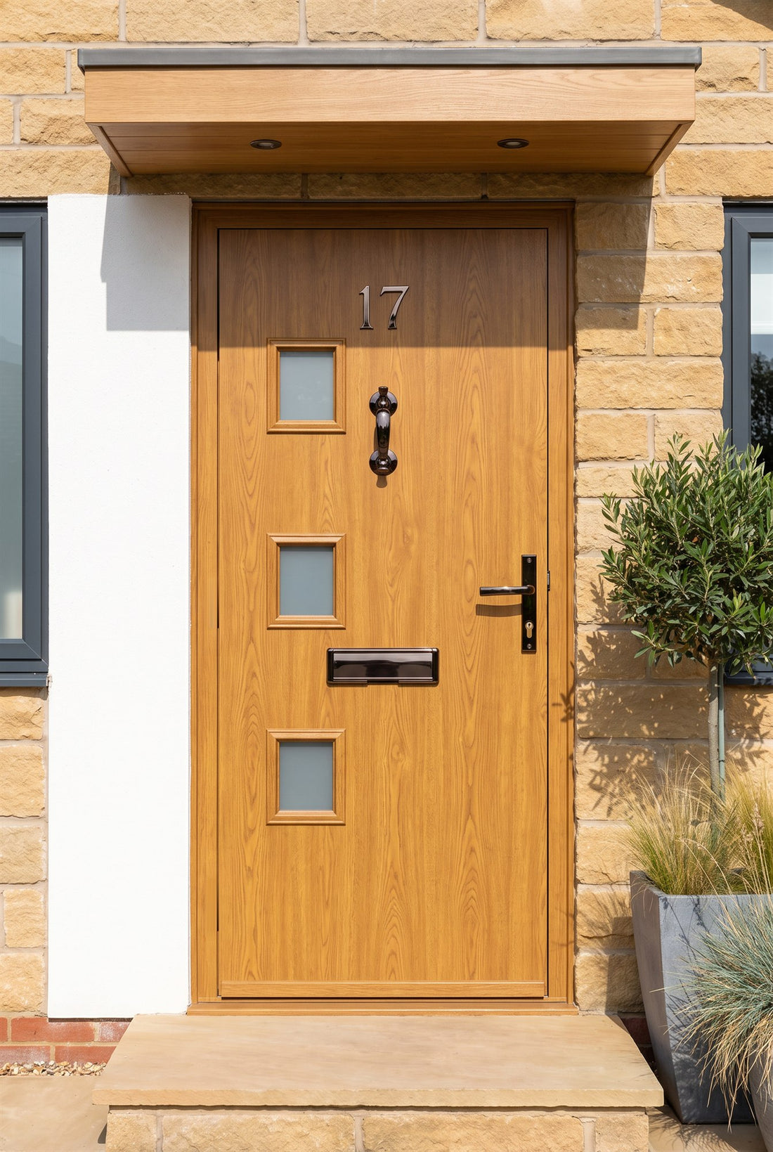 Golden oak woodgrain composite front door with three small frosted windows in a sandstone bungalow, fitted with Hardex bronze number 17, doctor knocker, Nu Mail shield letter plate and architectural lever