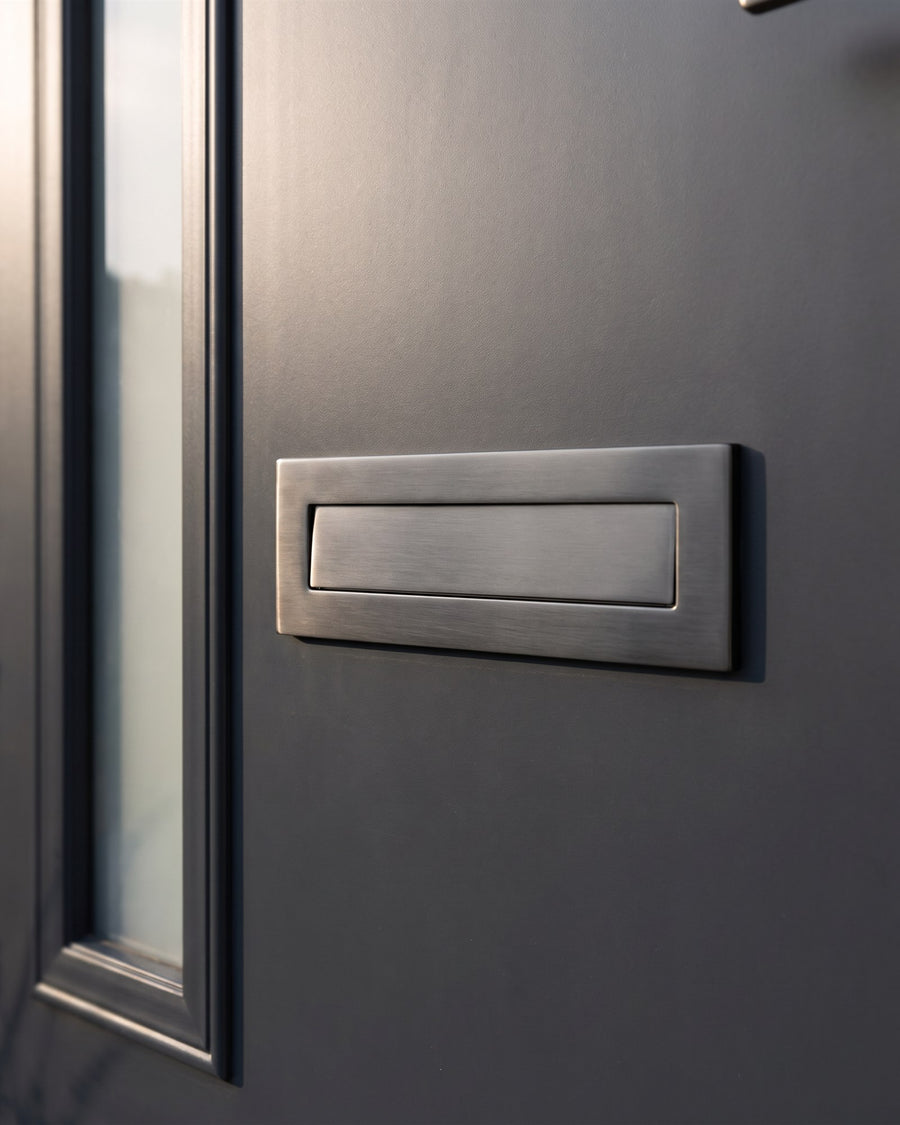 Graphite architectural shield letter plate on an anthracite composite door in low afternoon sun