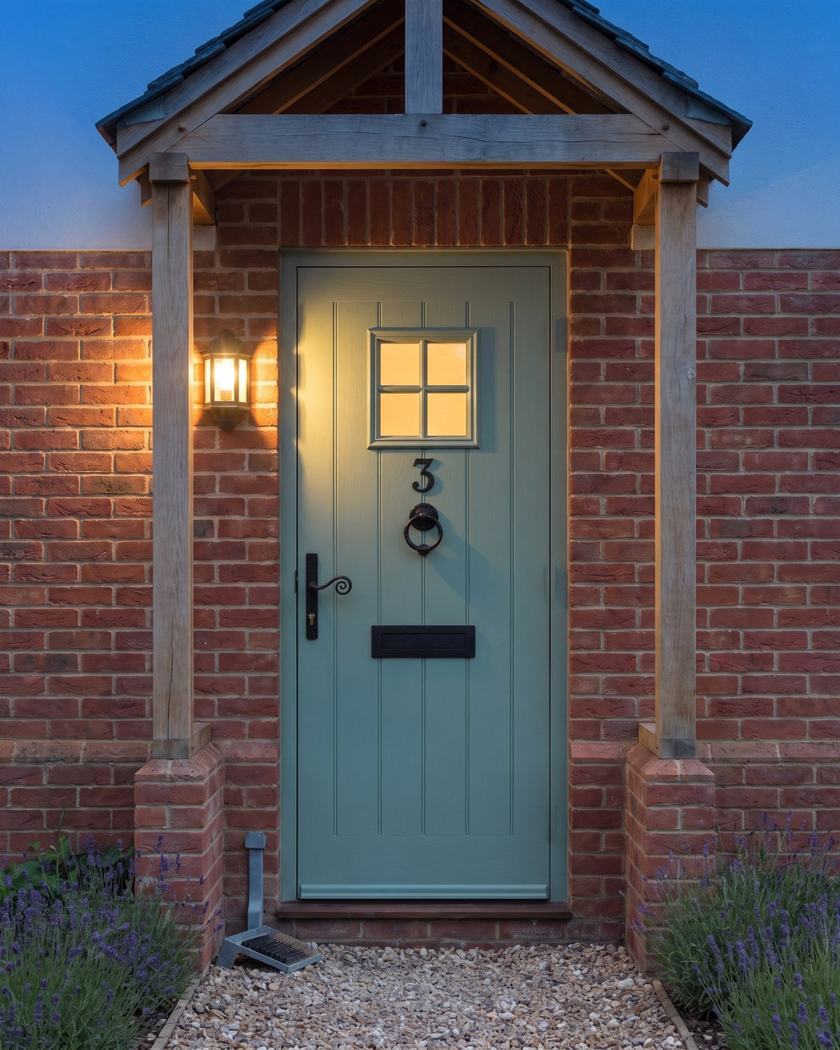 Heritage green cottage door under an oak porch at dusk, a black lantern glowing and forged black fittings silhouetted against the door