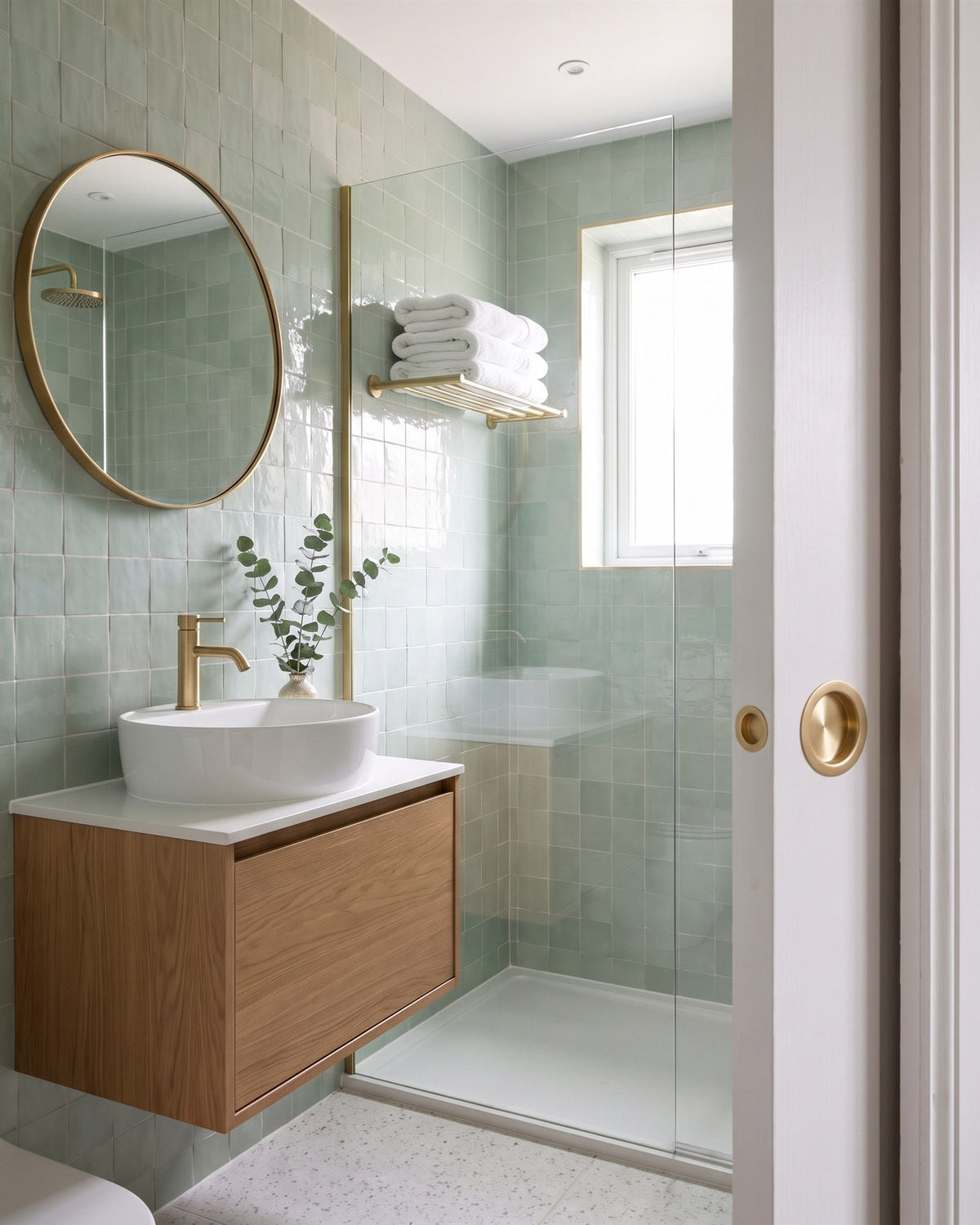 Green zellige en suite with an oak vanity and walk-in shower, seen past a white pocket door with a satin brass circular flush pull