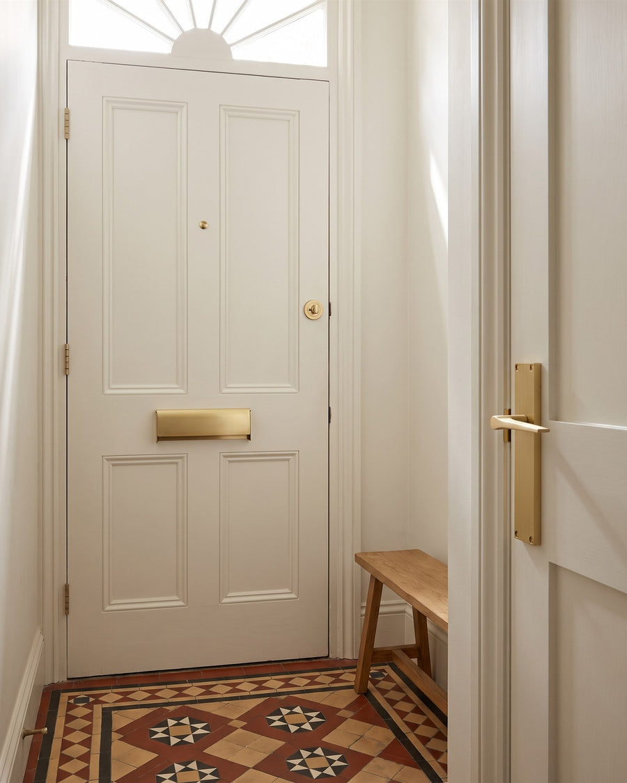 Victorian hallway with encaustic floor tiles, a satin brass letter tidy on the inside of the white front door and a Gio reeded lever on the hall door