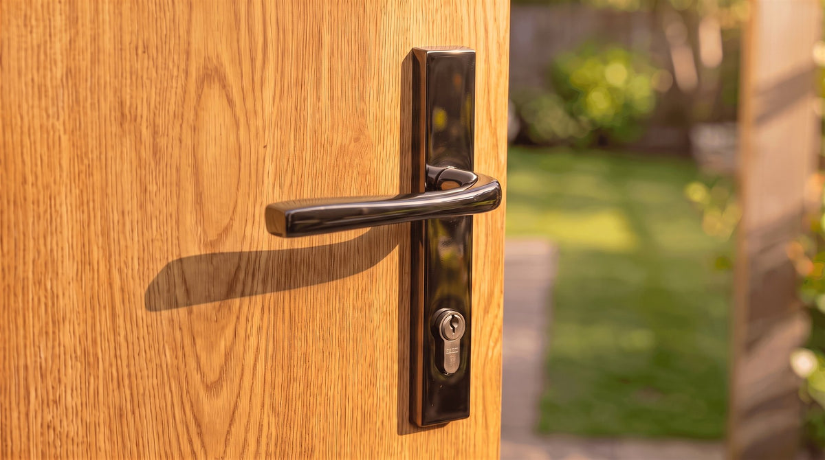 Hardex bronze architectural lever on a long backplate with a euro cylinder, its flattened grip widening towards the tip and curving back in towards a golden oak woodgrain composite door