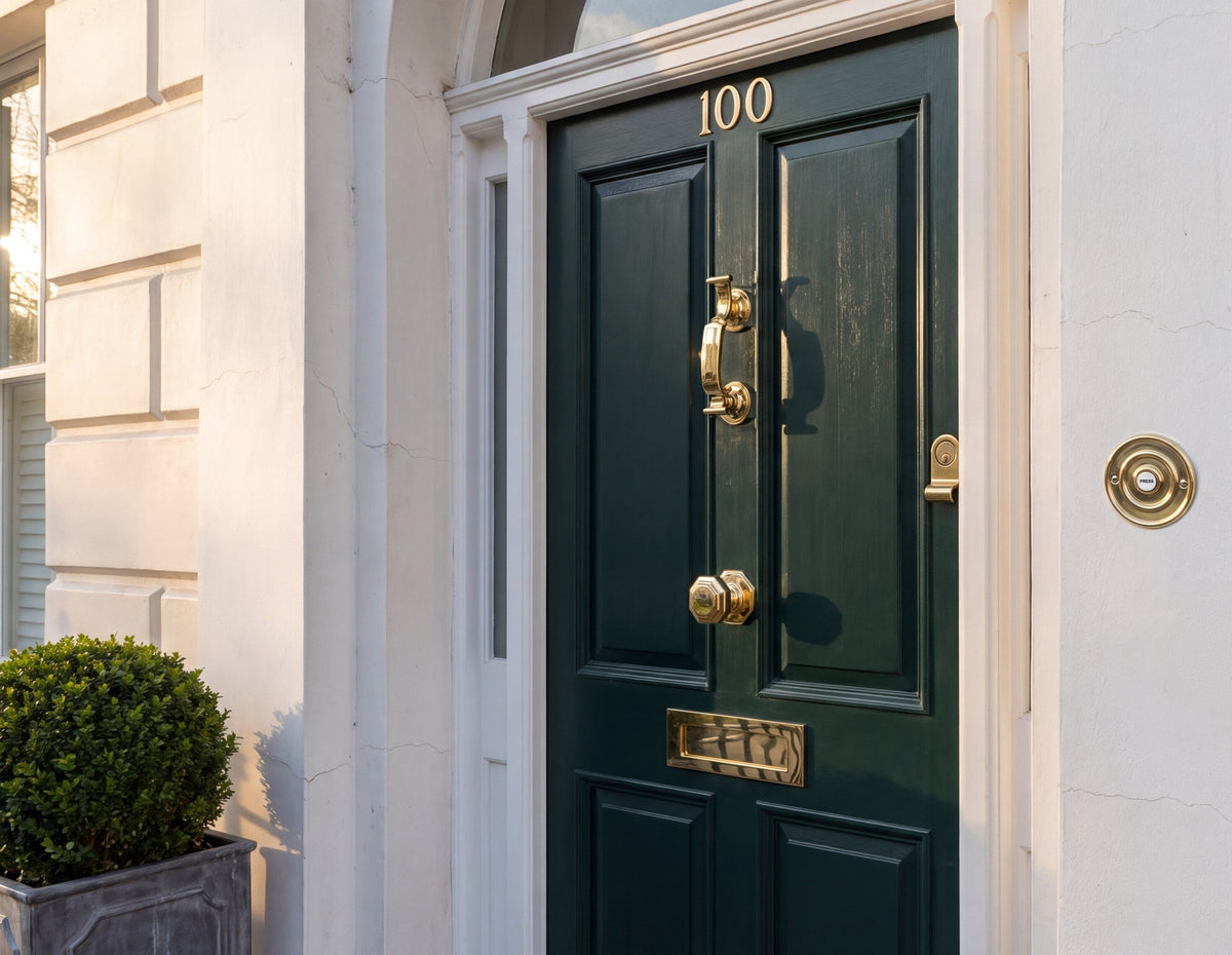 Dark green front door with a polished brass knocker, octagonal centre knob, letter plate and house numbers