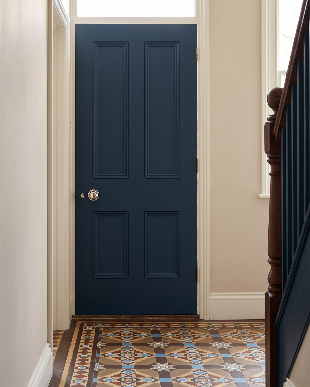 Ink blue panelled door off a stone coloured hallway with encaustic tiles, fitted with a polished nickel mushroom knob