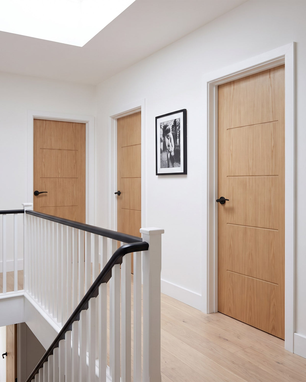 Bright landing with a roof light, white balustrade with black handrail and a run of oak veneer doors with matt black levers and hinges