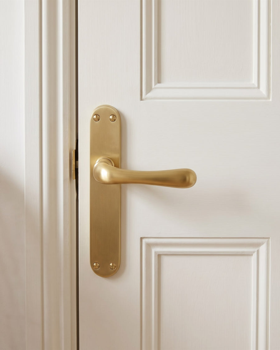 Luna satin brass lever on a slim rounded backplate on a warm white panelled door