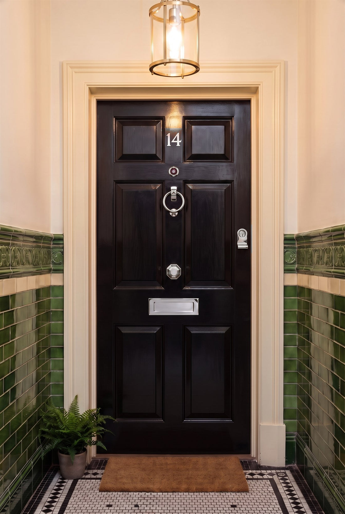 Glossy black six-panel flat door in a tiled mansion block corridor, fitted with polished chrome number 14, door viewer, ring knocker, octagonal centre knob, letter plate and cylinder pull