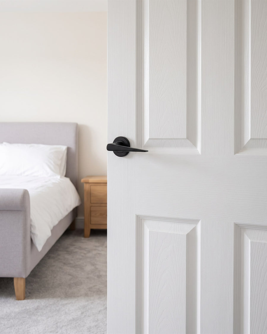 Matt black Amalfi lever on rose on a white bedroom door opening onto a grey upholstered bed