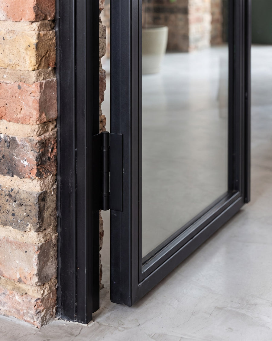 Matt black flush hinge on the slim steel frame of a black glazed door against exposed brick
