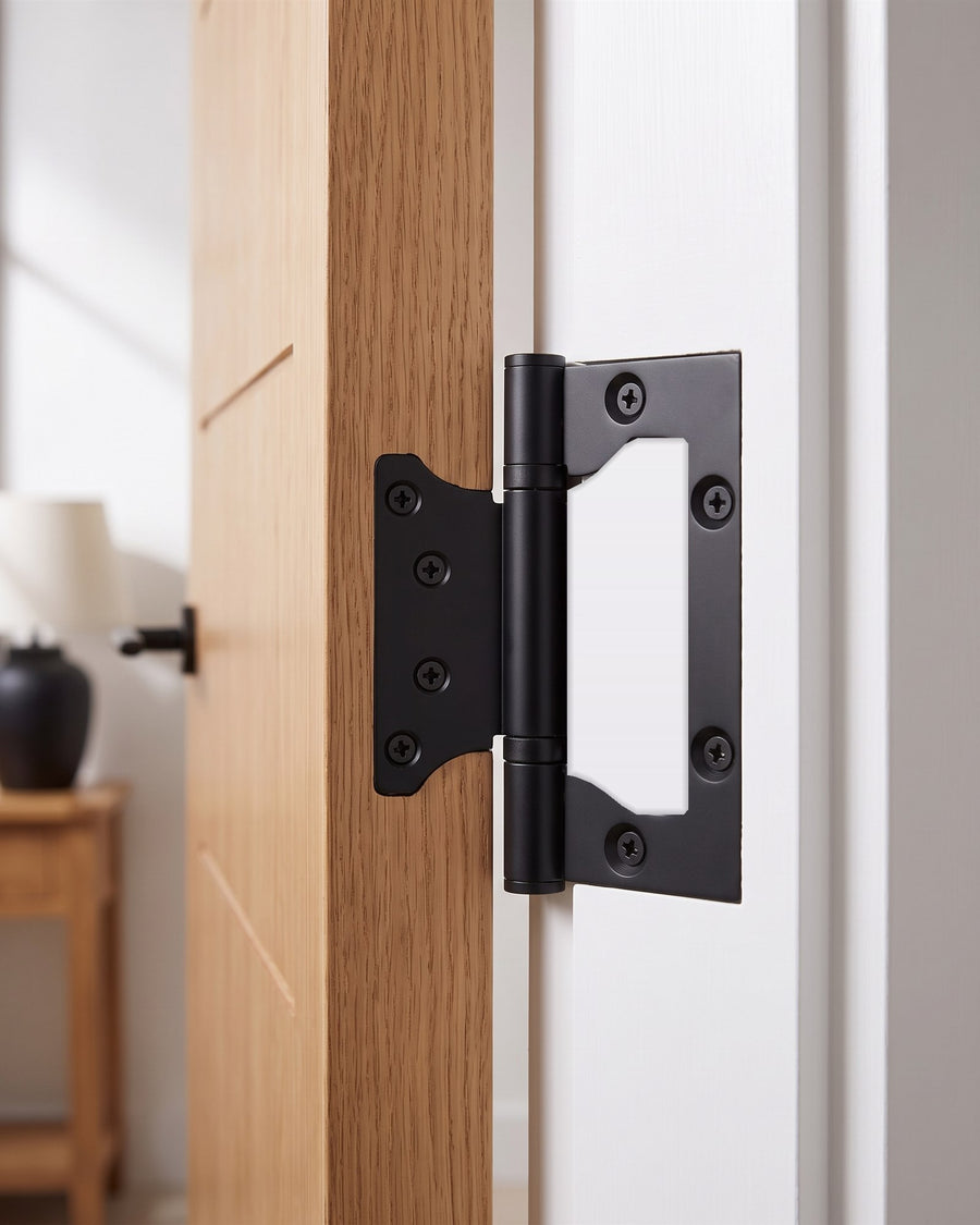 Matt black flush hinge fixed to the edge of an oak veneer door and a white frame