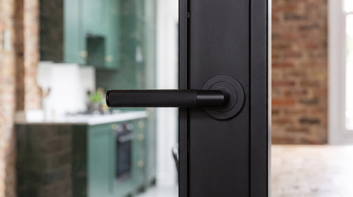 Matt black knurled lever on rose on the slim stile of a black-framed glazed internal door