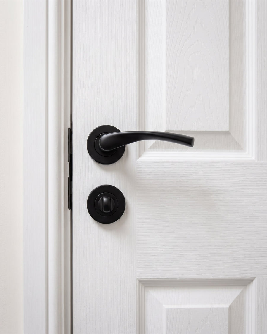 Matt black lever on rose above a matt black turn and release on a white moulded bathroom door