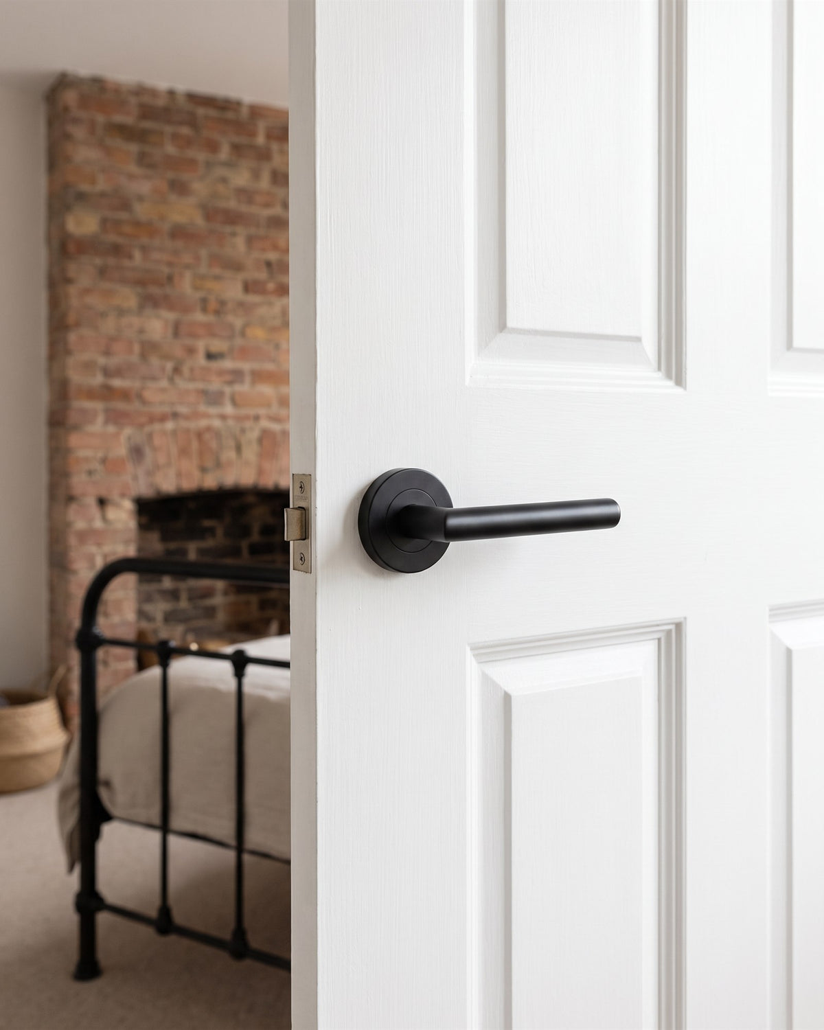Matt black Shuttle lever on rose on a white bedroom door, exposed brick chimney breast and iron bed beyond