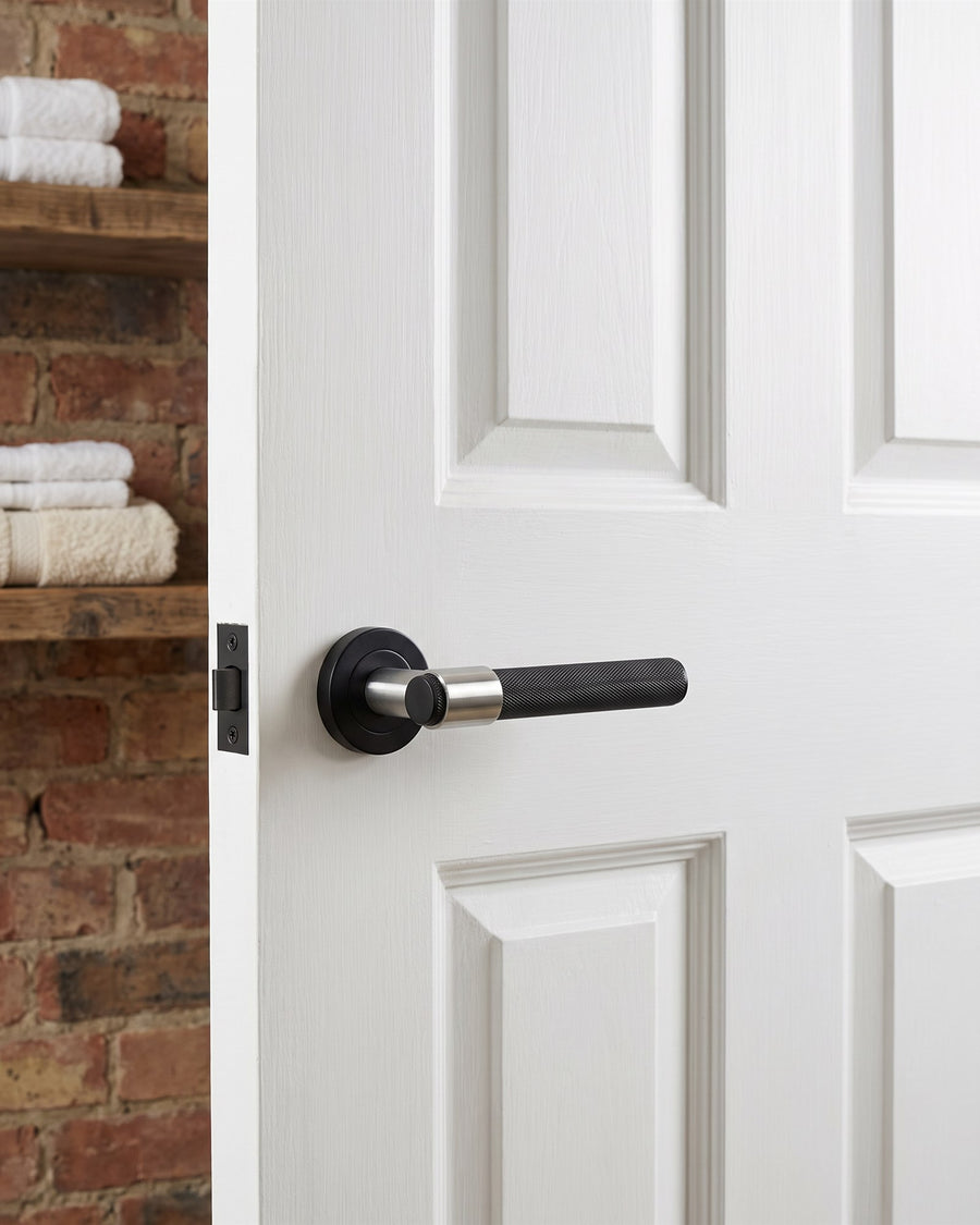 Matt black T-bar knurled lever on a white panelled utility room door beside an exposed brick wall