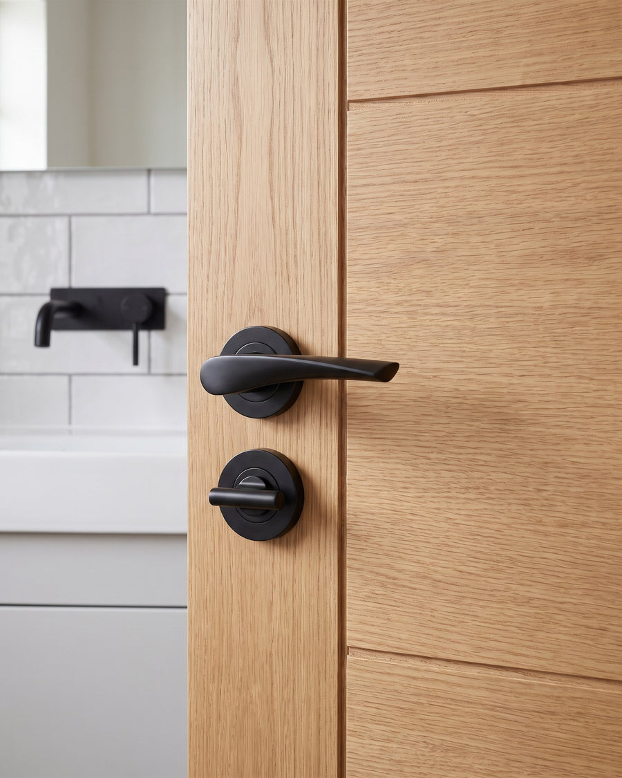 Matt black Vecta lever above a matt black easy turn on an oak veneer bathroom door, white tiles and a black tap beyond