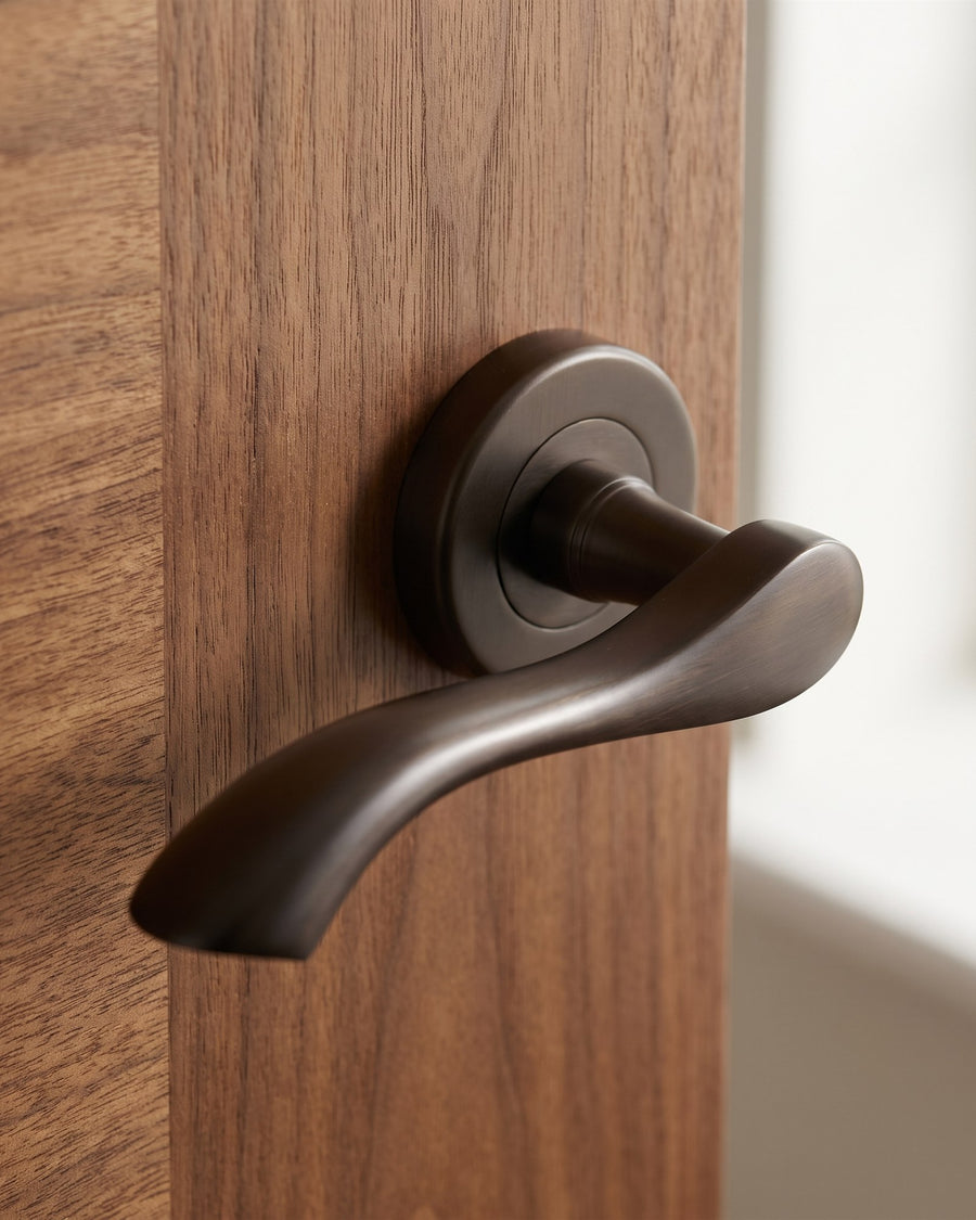 Close-up of a matt bronze Algarve lever on rose on a walnut veneer door, showing the twisting sculpted lever