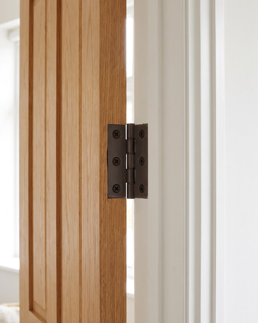 Matt bronze butt hinge on the edge of a golden oak door and white frame