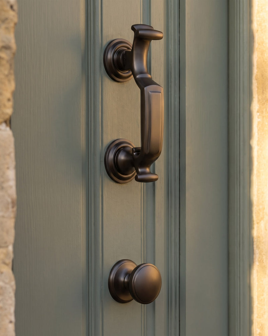 Matt bronze doctor knocker above a matt bronze centre knob on a sage green front door in warm low sun