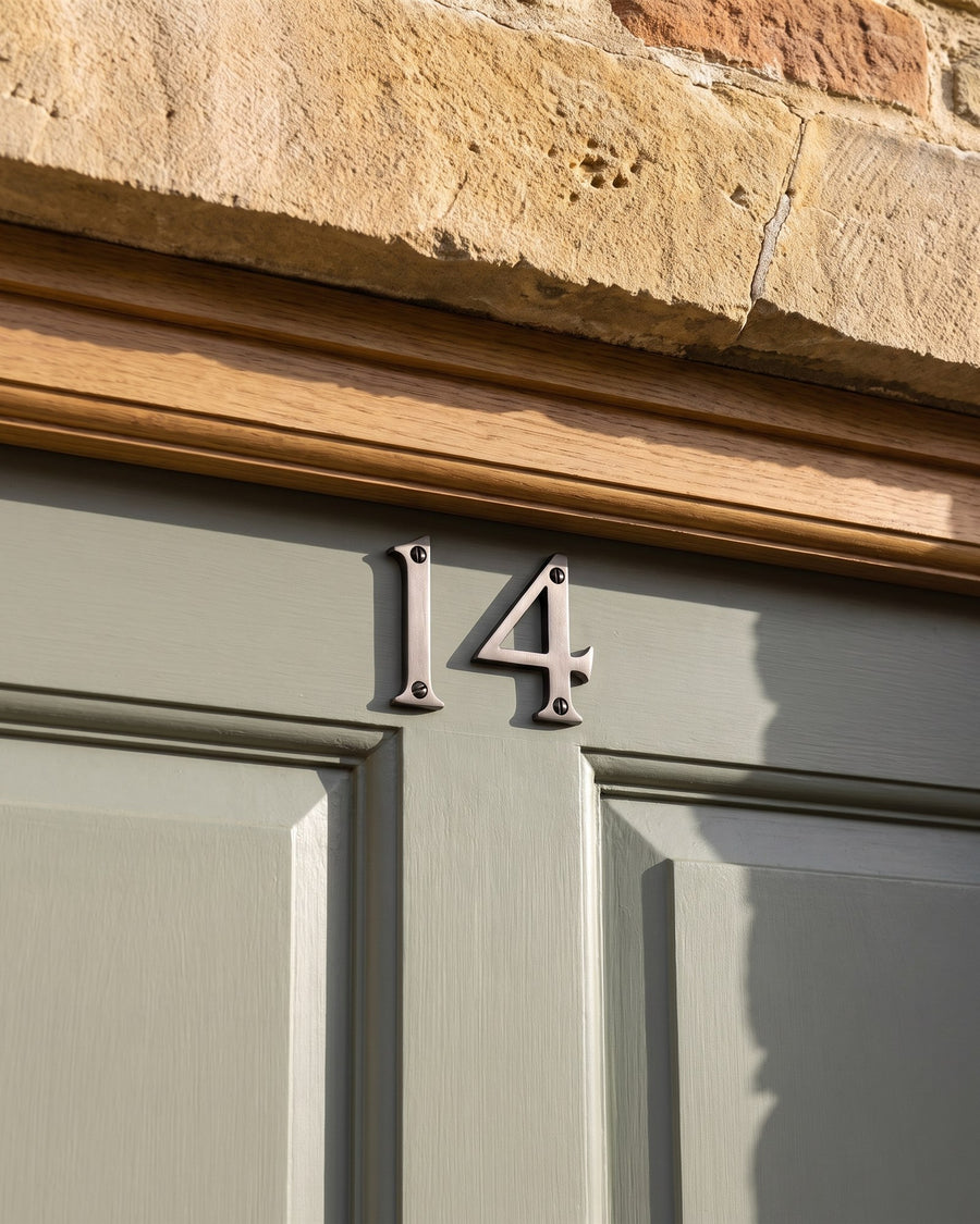 Matt bronze house numbers on the top rail of a sage green front door below an oak head and stone lintel