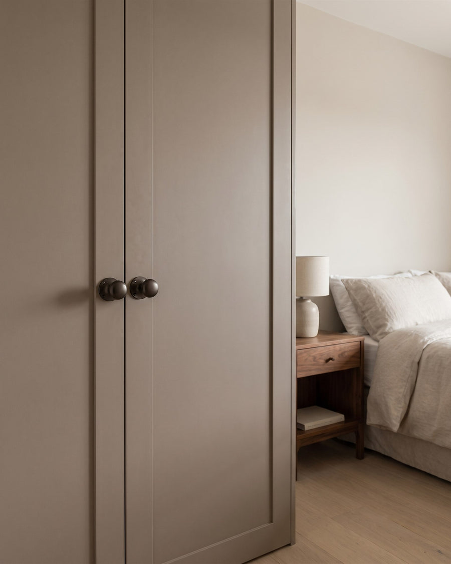Mushroom-painted fitted wardrobe doors with matt bronze Kensington mortice knobs in a calm bedroom with linen bedding