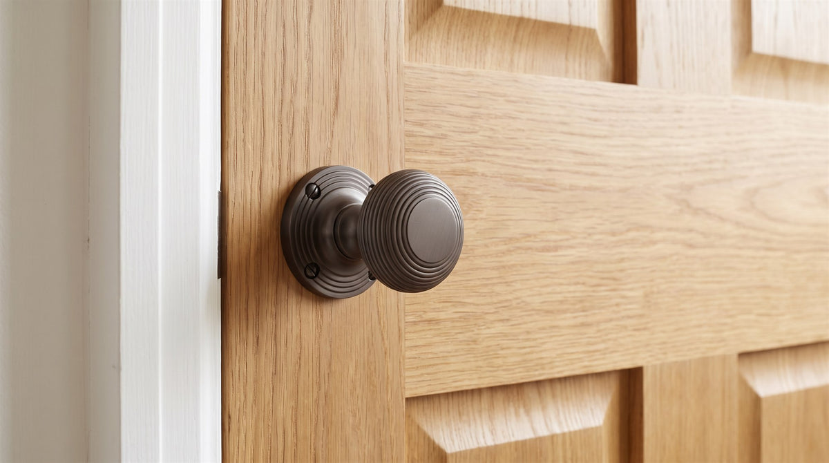 Matt bronze reeded mortice knob with stacked concentric rings on a reeded rose, on a natural oak four-panel door