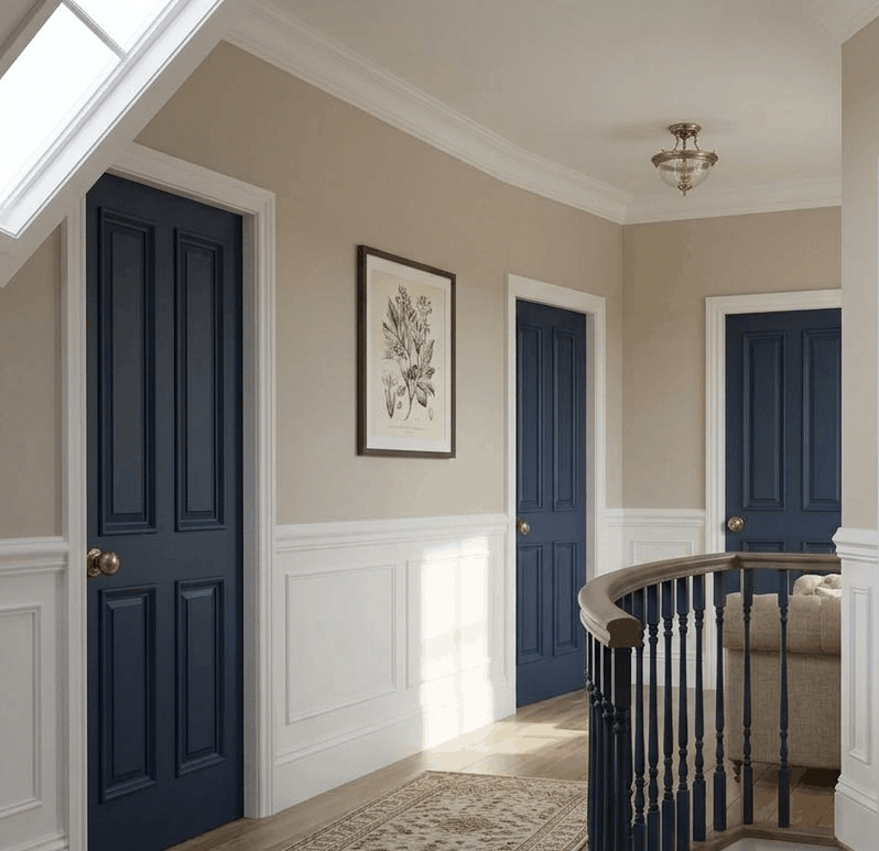 Landing with navy blue panelled doors in white architraves, putty walls above white panelling and a dark painted banister, each door with a small brass knob