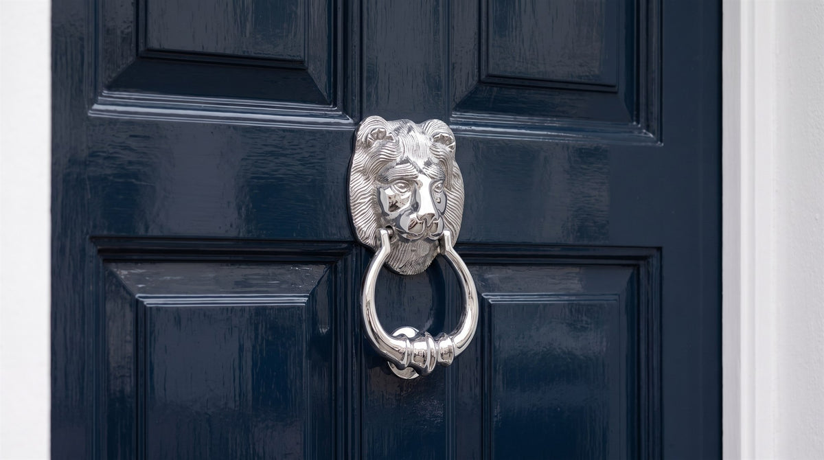 Polished chrome lion head knocker on a navy gloss six-panel front door in a white stucco portico