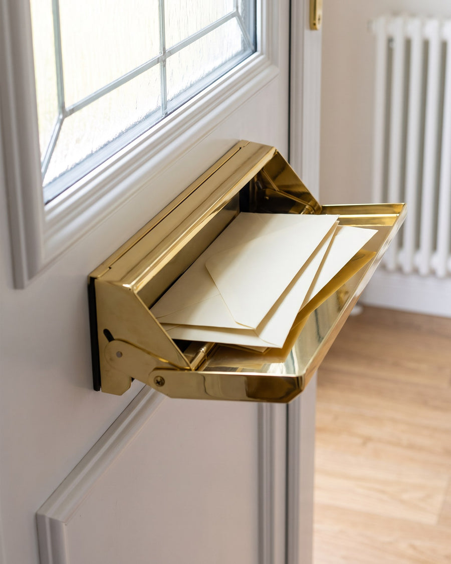 Gold Nu Mail internal shield hood with envelopes inside, on the inside of a white uPVC front door below the leaded glass