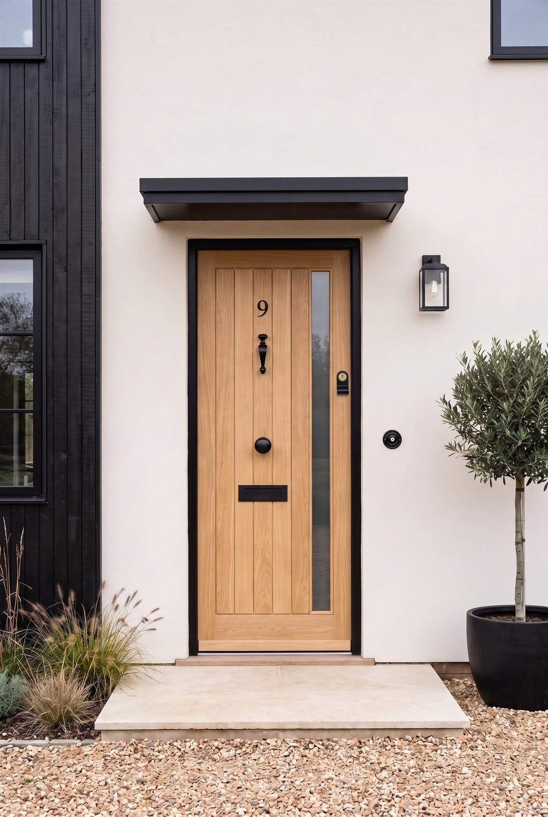 Natural oak boarded front door with a glazed strip under a black canopy, fitted with matt black number 9, doctor knocker, centre knob, letter plate, cylinder pull and round bell push