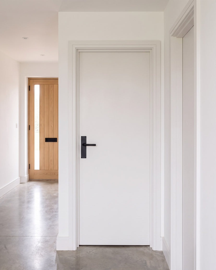 Octave matt black lever on a slim backplate on a white flush internal door, with the oak front door at the end of the hall