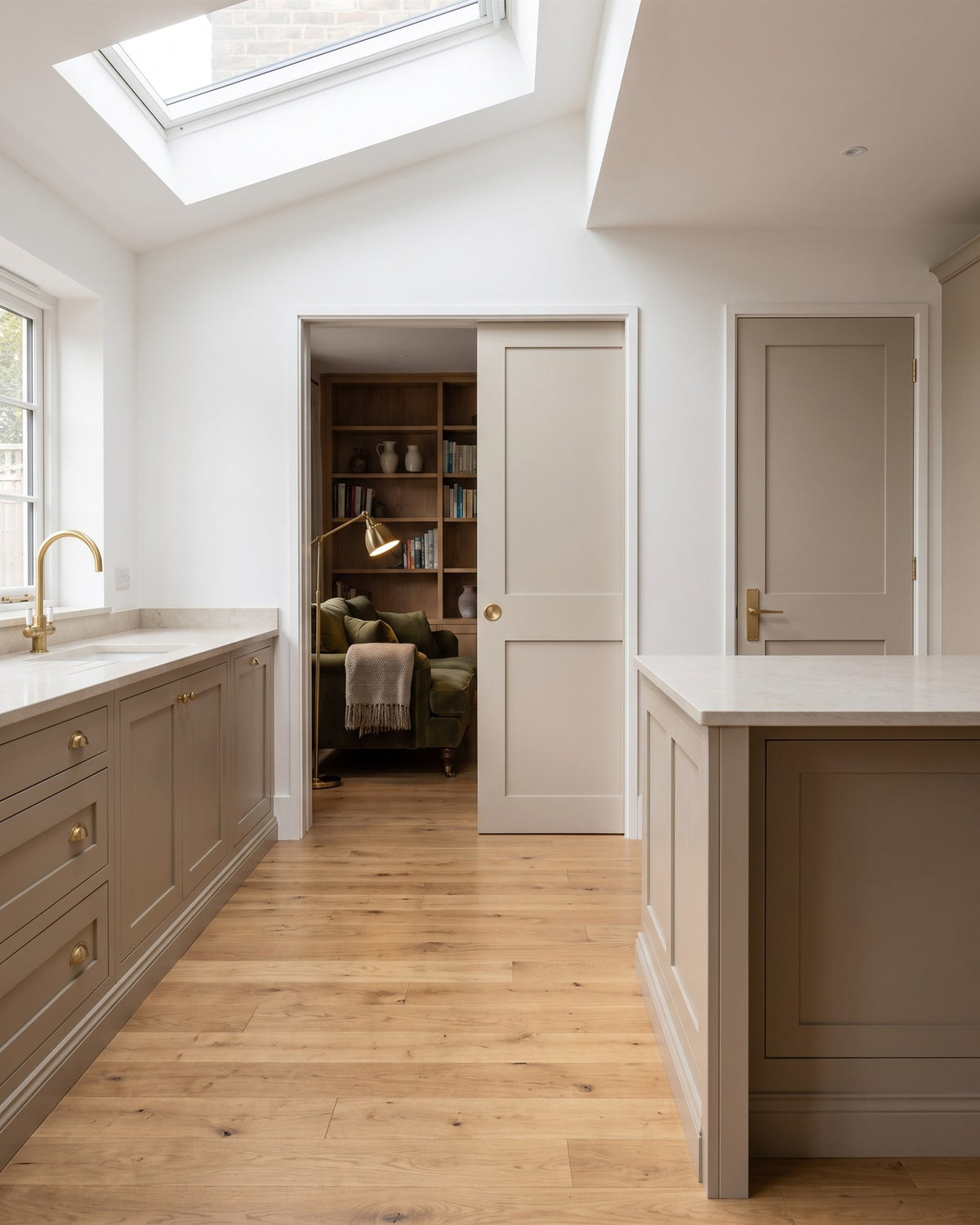 Open-plan kitchen extension with putty painted units, oak floor and a rooflight, a pocket door half open to a snug and a hinged door with a satin brass lever
