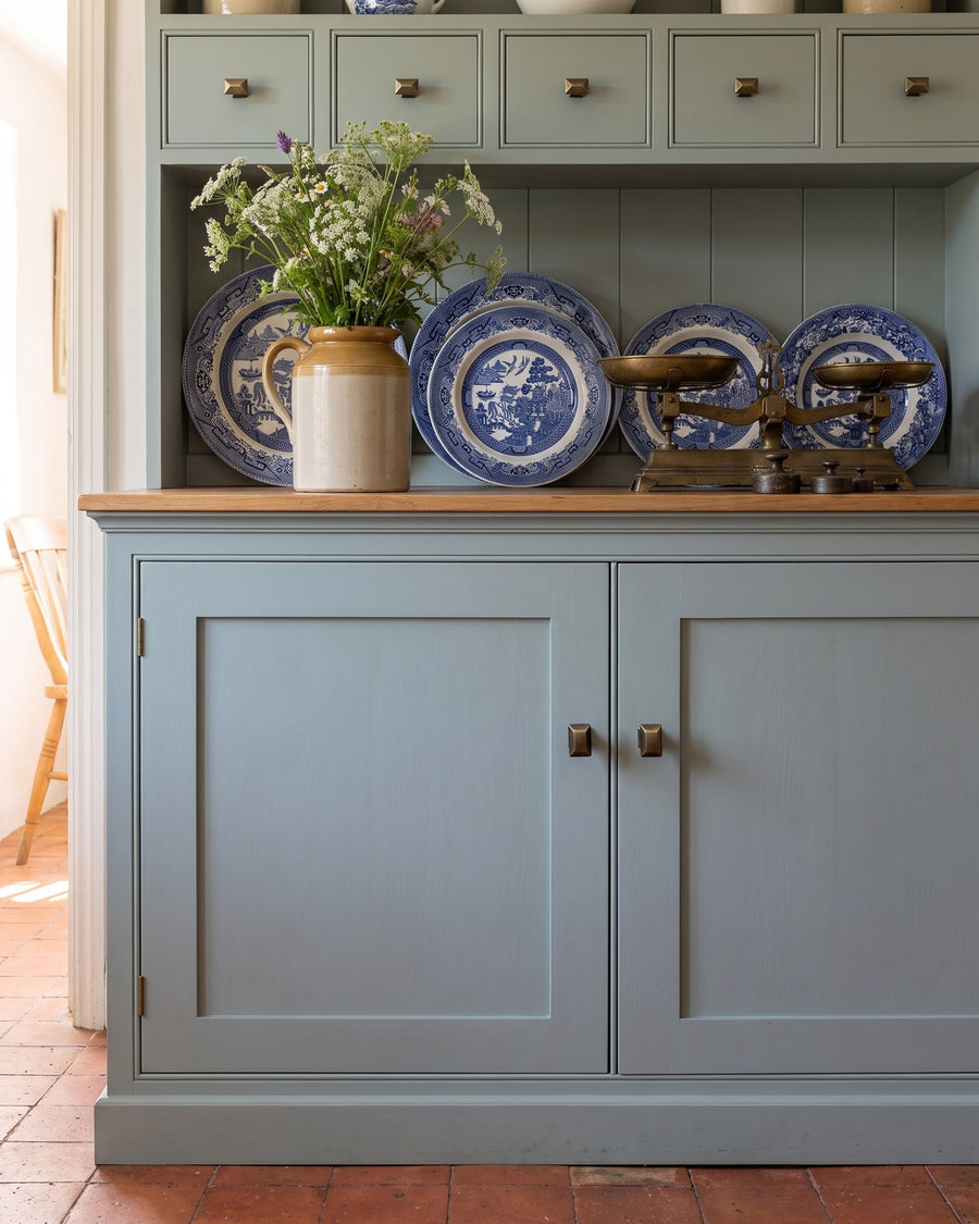 Painted kitchen dresser with small spice drawers and cupboard doors fitted with antique brass anvil knobs, blue and white plates on the shelf