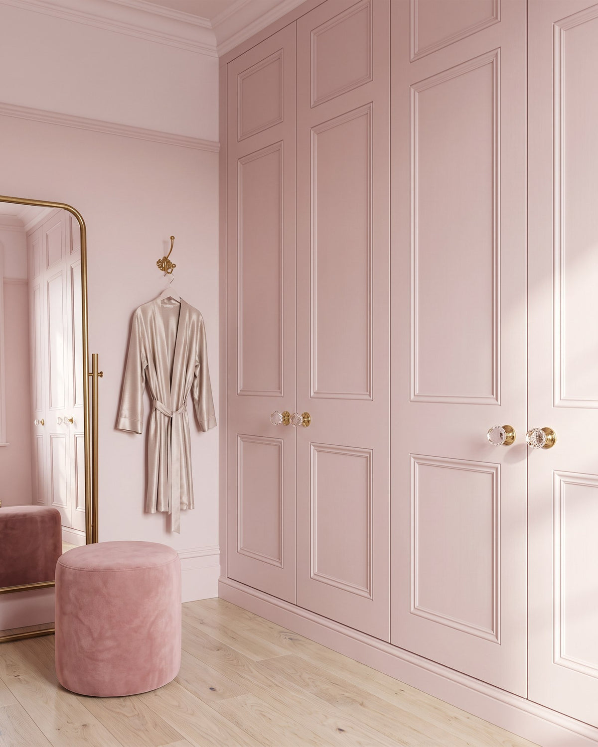 Dressing room with pink panelled wardrobes fitted with cut glass knobs, a velvet pouffe, a brass-framed mirror and a silk robe on a brass hook