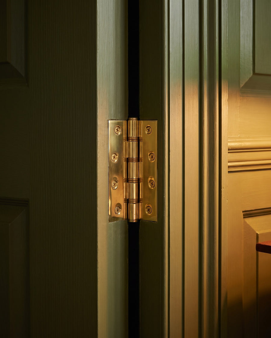 Polished brass butt hinge on the edge of an olive green panelled study door
