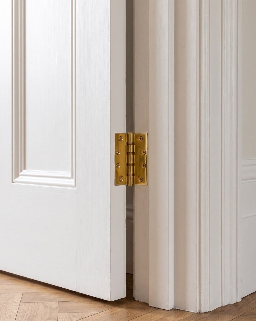 Polished brass butt hinge on a tall white panelled door above oak parquet