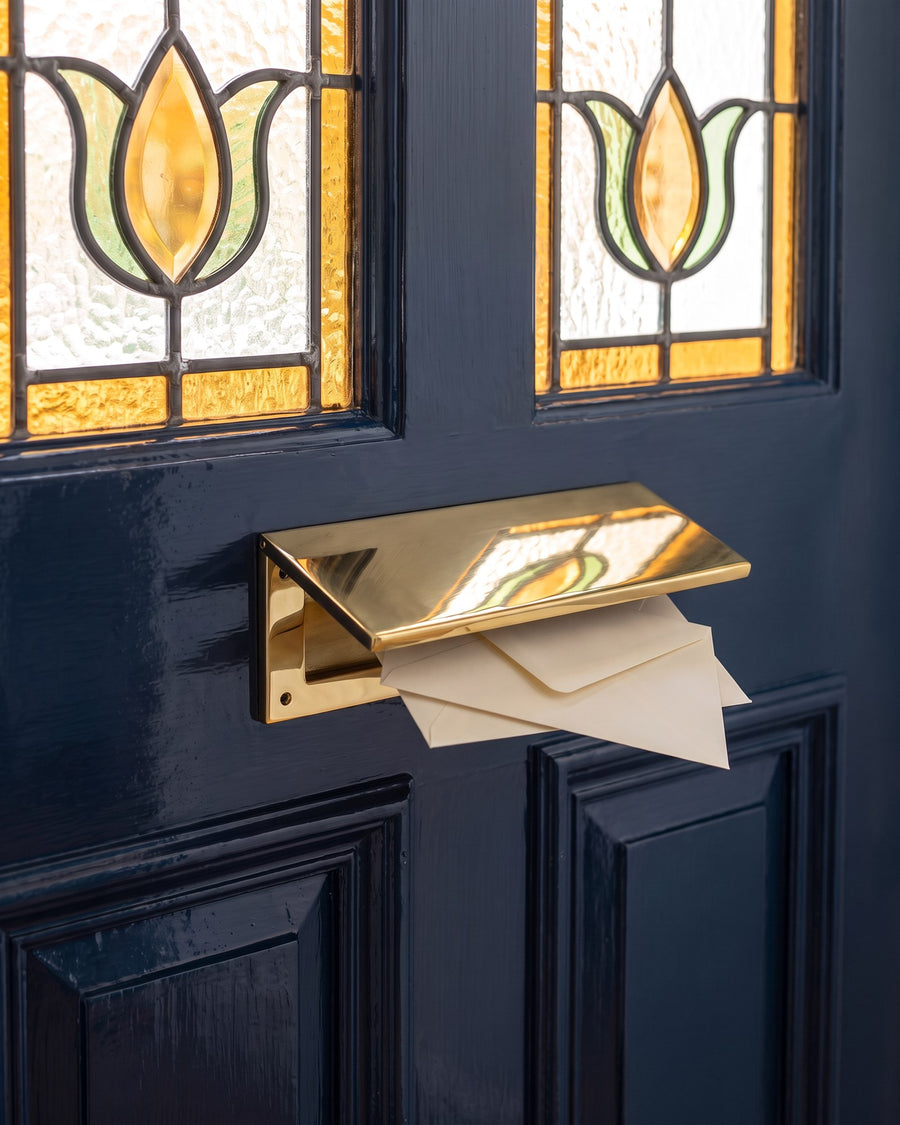 Polished brass internal tidy holding two cream envelopes on the inside of the inky blue door below the tulip stained glass