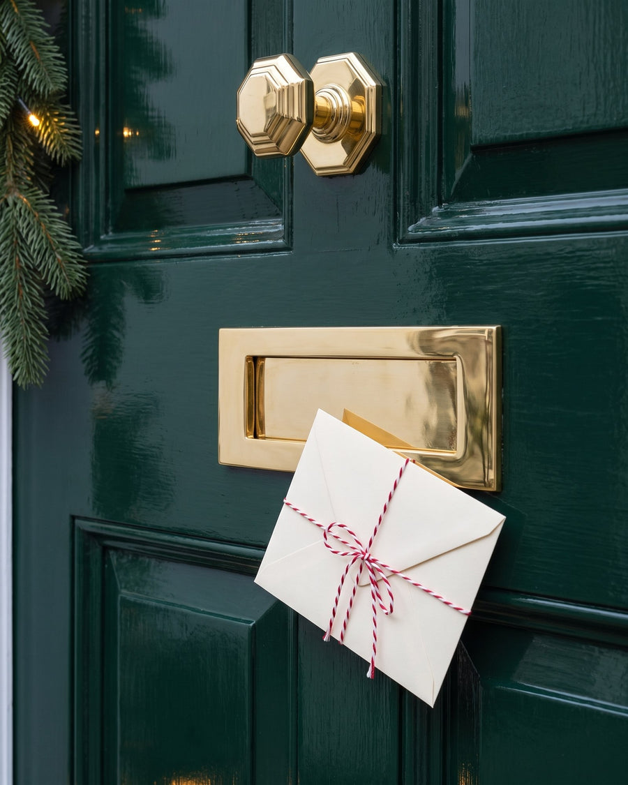 Polished brass Victorian letter plate on a bottle-green door with a Christmas card tied in red and white twine, the octagonal brass knob above