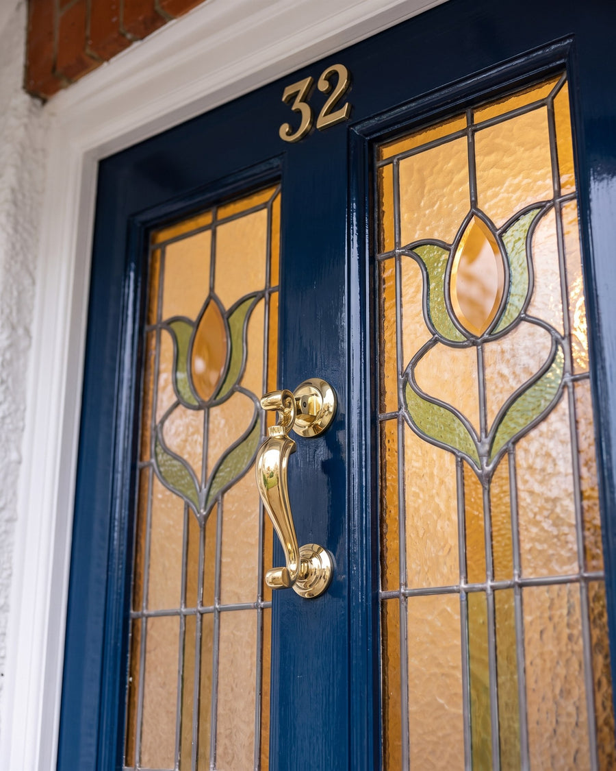 Polished brass serif number 32 above a polished brass profile doctor knocker between amber and green tulip stained-glass panels on an inky blue door