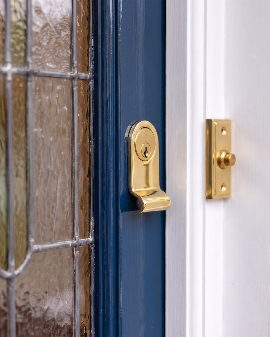 Polished brass radiused cylinder pull with a brass euro cylinder on a blue door beside a polished brass rectangular bell push on the white frame