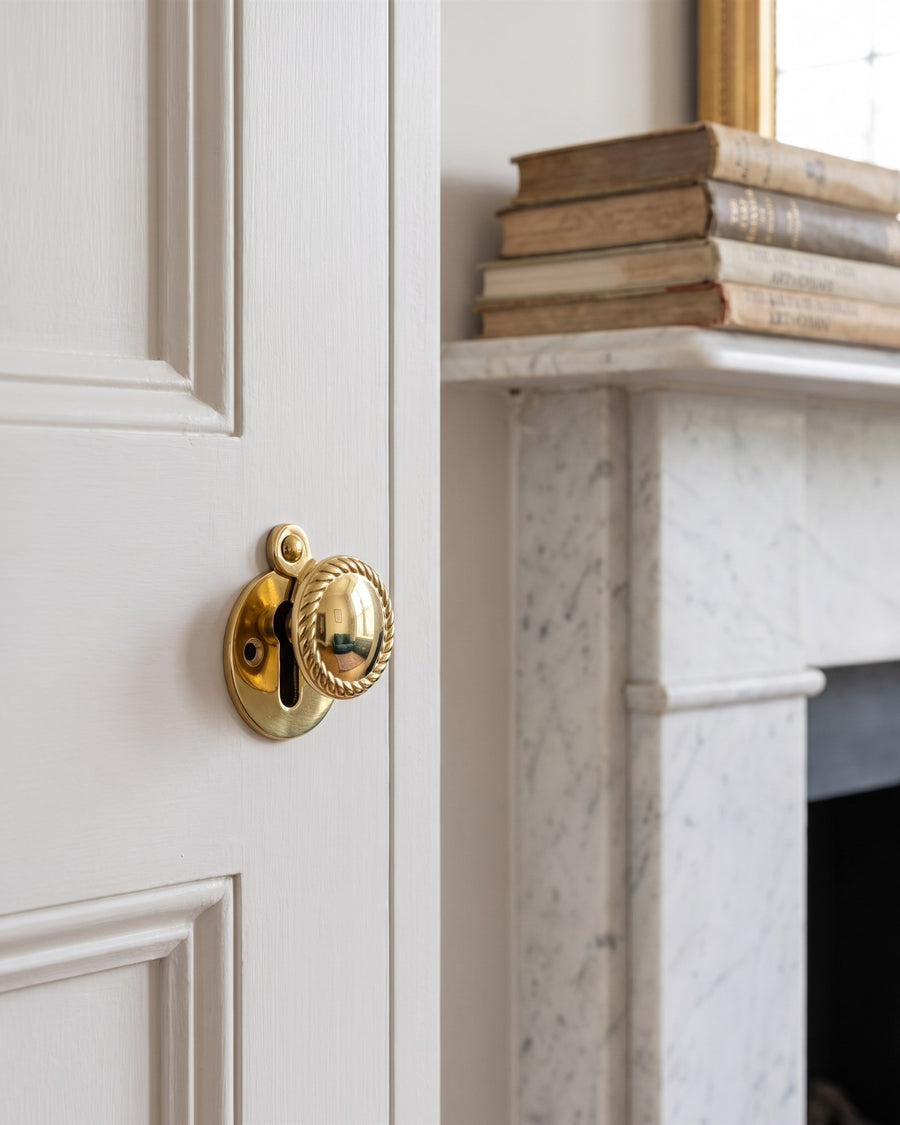 Polished brass covered escutcheon with a rope edge on a white alcove cupboard door beside a marble fireplace